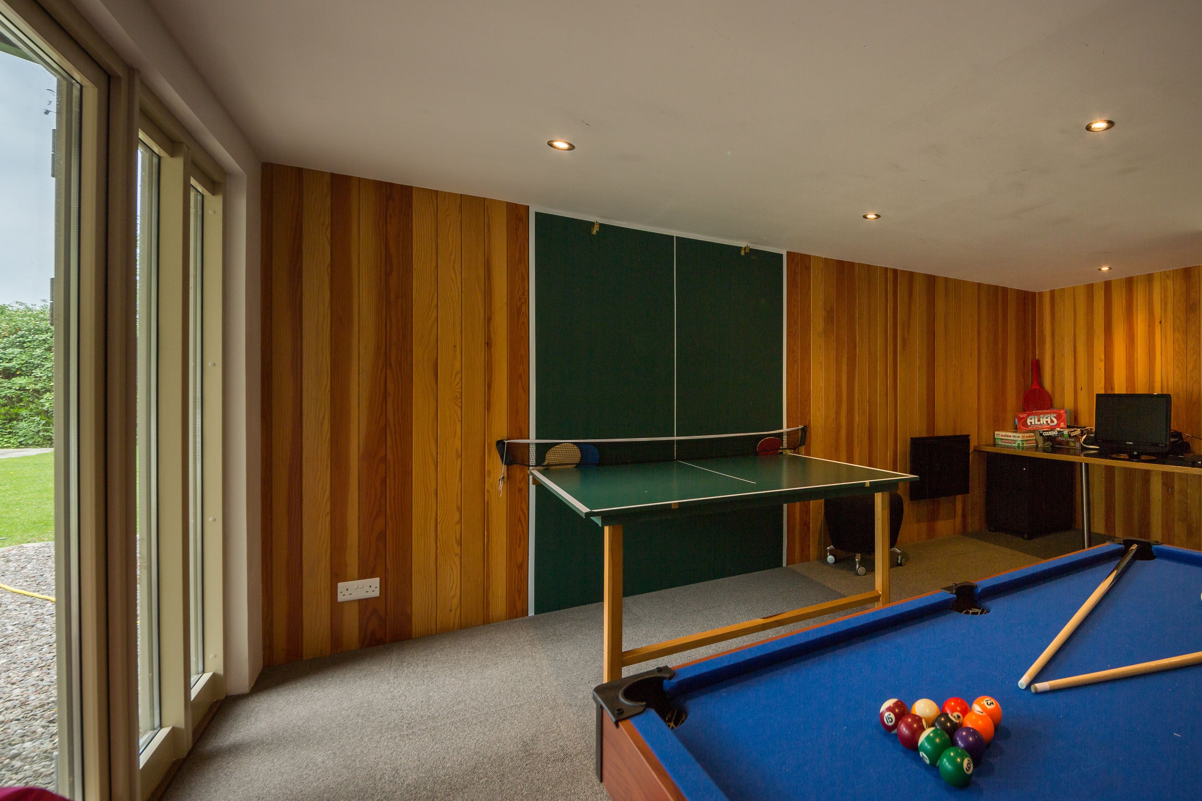 A billiards room with a pool table, a green table tennis table, and a television.