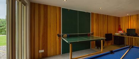 A billiards room with a pool table, a green table tennis table, and a television.