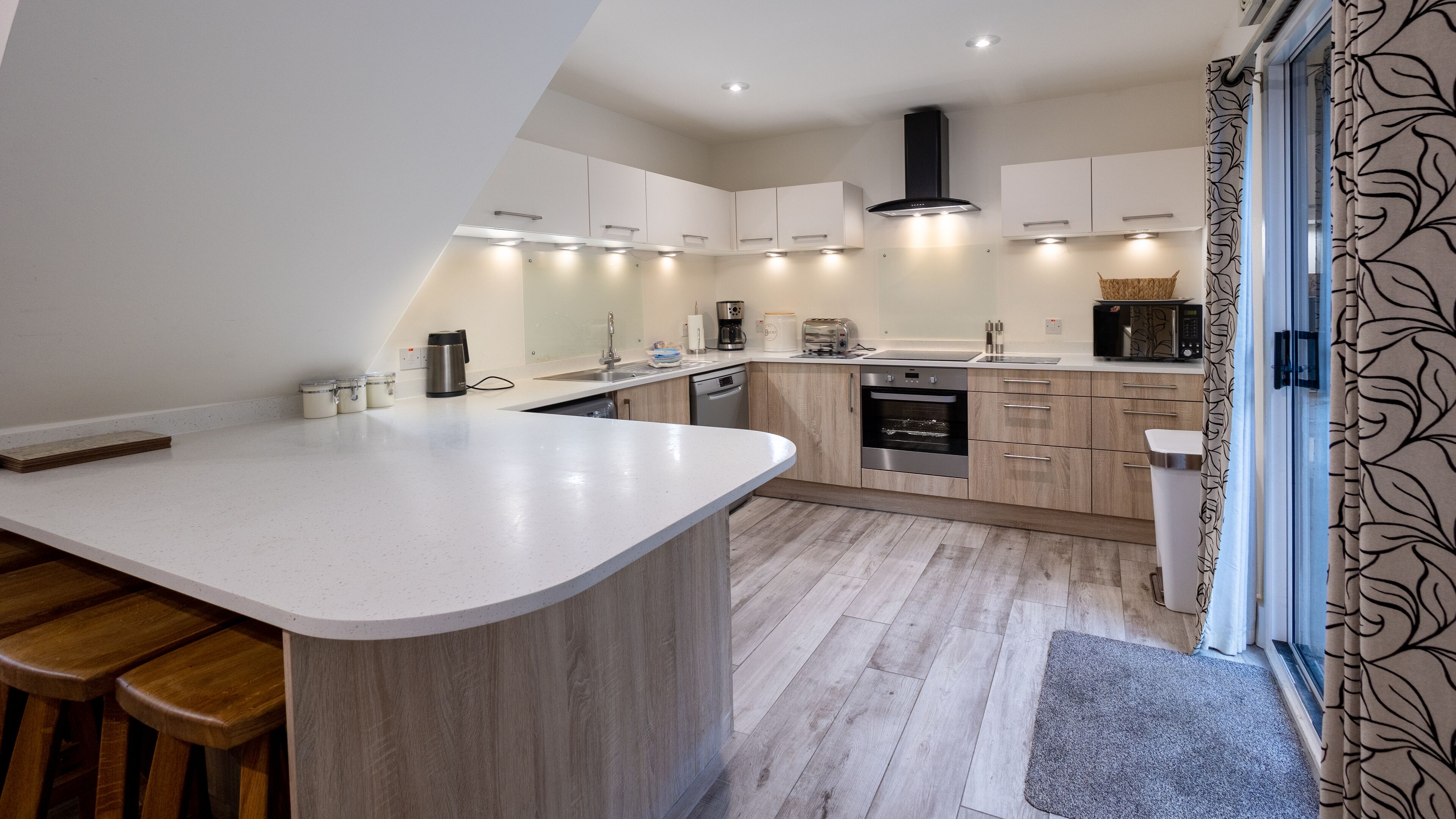A modern kitchen with a central island, built-in appliances, and a large window with patterned curtains.