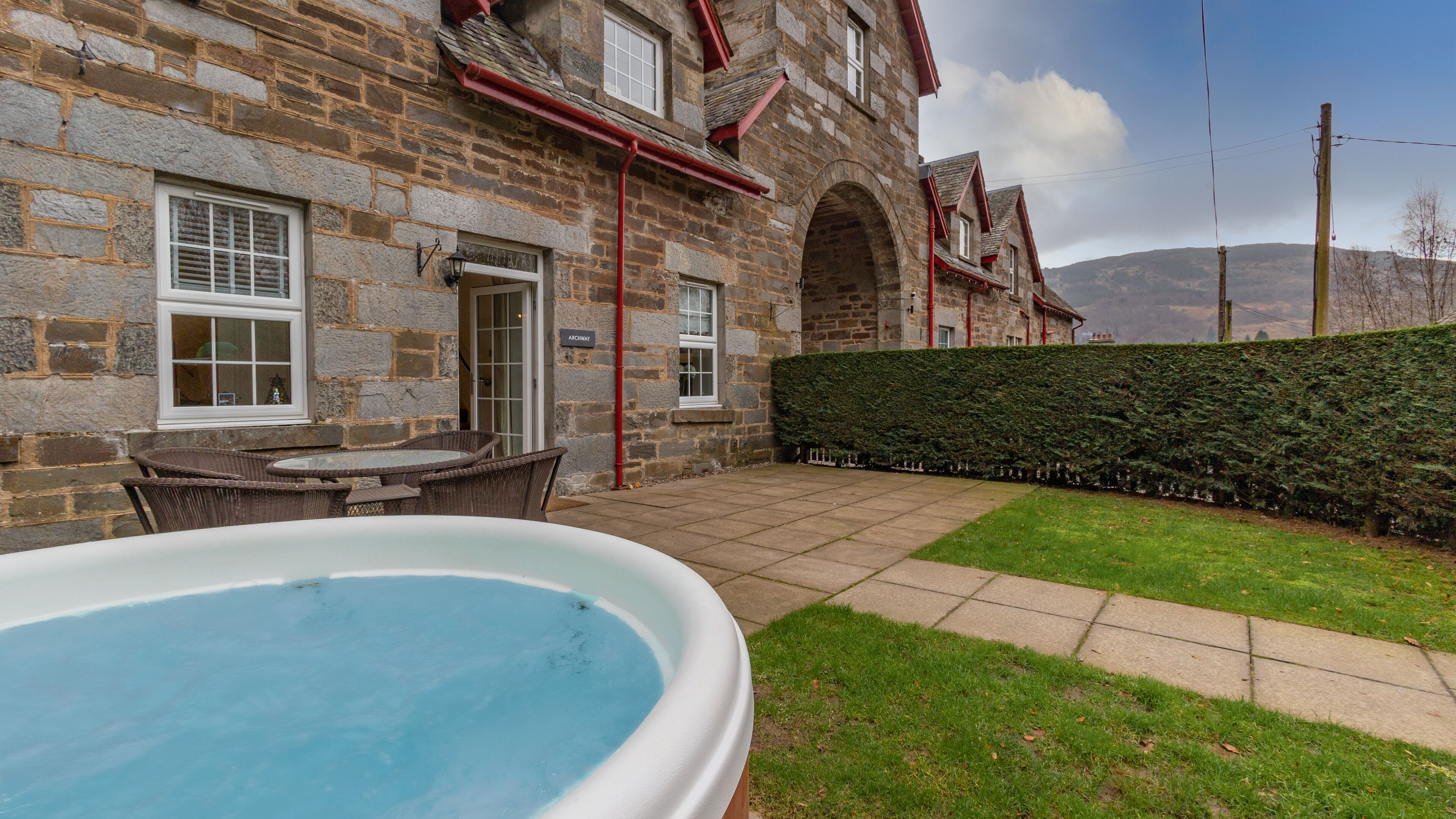 A stone building with a patio, a swimming pool, and a hedge.