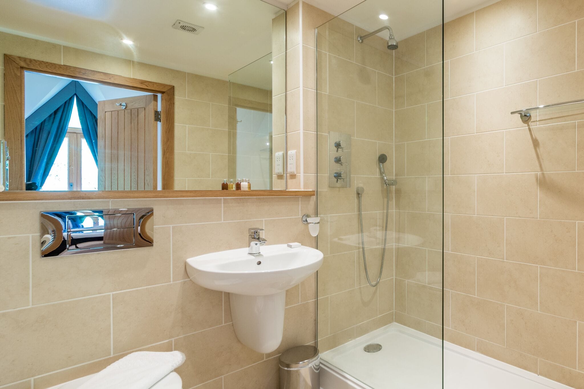 Een moderne badkamer met een douchecabine van glas, een wastafel op een voetstuk en een grote spiegel boven de wastafel.