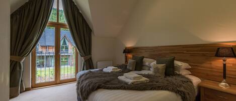 A bedroom with a large bed, wooden headboard, and a view of a wooden cabin through a window with curtains.