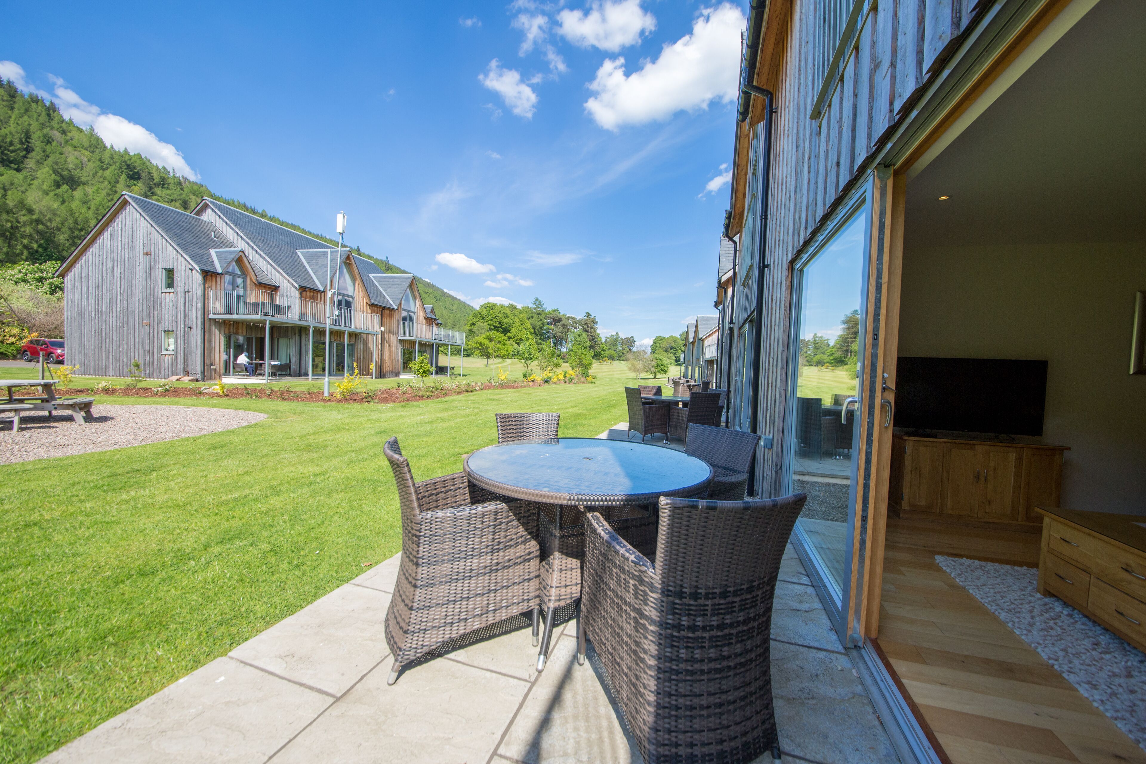 Une terrasse avec des meubles en osier, une pelouse et une grande maison en arrière-plan.
