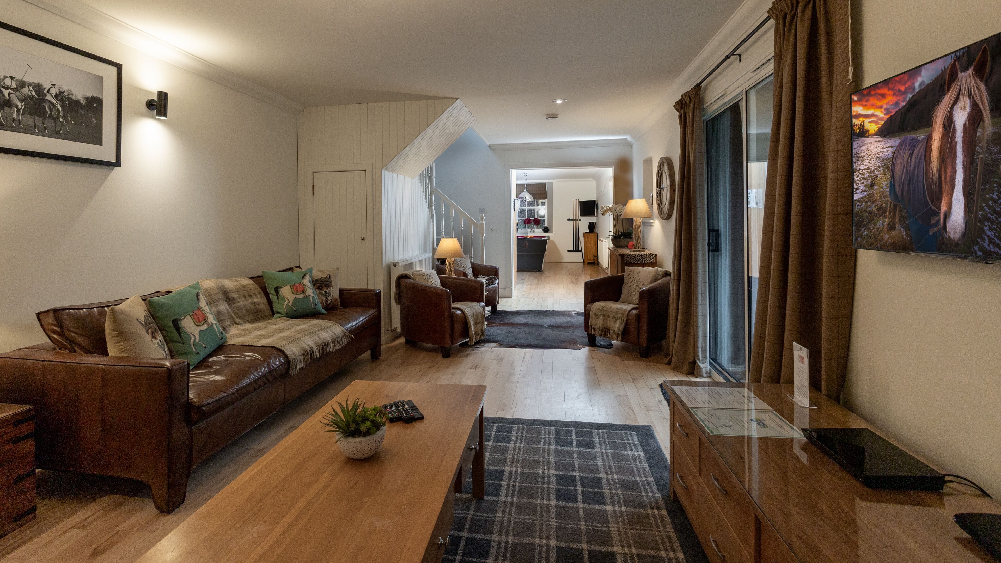 Een woonkamer met een bruine leren bank, een houten salontafel en een televisie aan de muur.