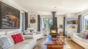 Un salon moderne doté d’une cheminée, de canapés en cuir et de grandes fenêtres offrant une vue sur l’extérieur.