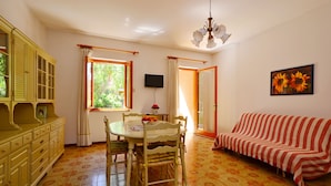 A dining area with a table and chairs, a sofa, and a television on the wall.