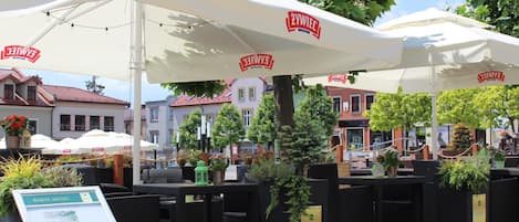 Outdoor seating with white umbrellas, a menu board, and potted plants.