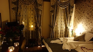 A hotel room with a bed, a desk with a vase of flowers, and curtains.
