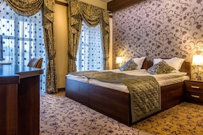 A hotel room with a large bed, a desk, and a patterned carpet. - Hotel-restauracja Platan (Chrzanow)