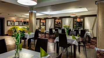 A hotel dining area with multiple tables, chairs, and a bar area.