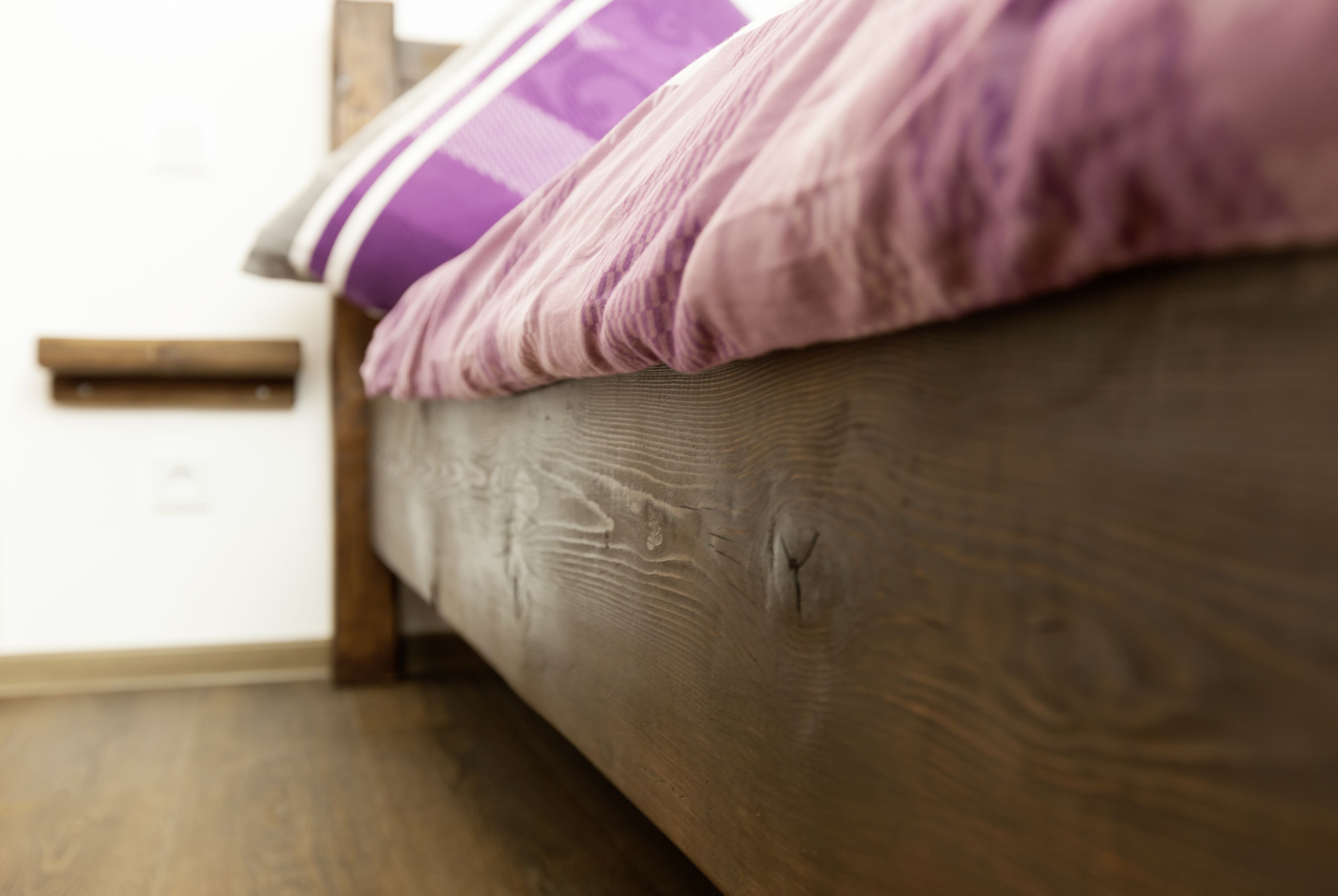A wooden bed with a textured surface and a purple pillow.