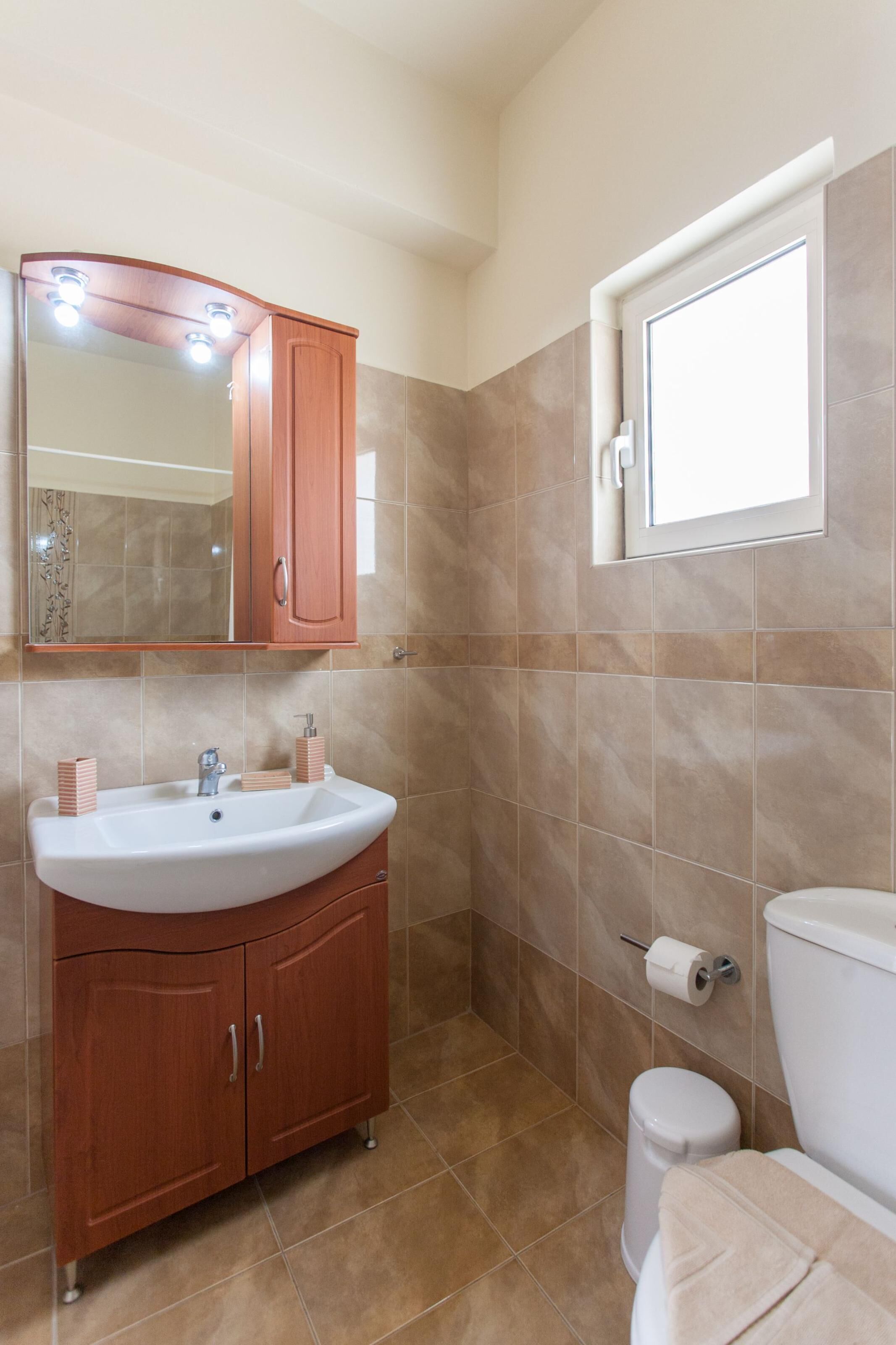Une salle de bain équipée d’un lavabo, d’un miroir, d’un meuble de rangement, de toilettes et d’une fenêtre.