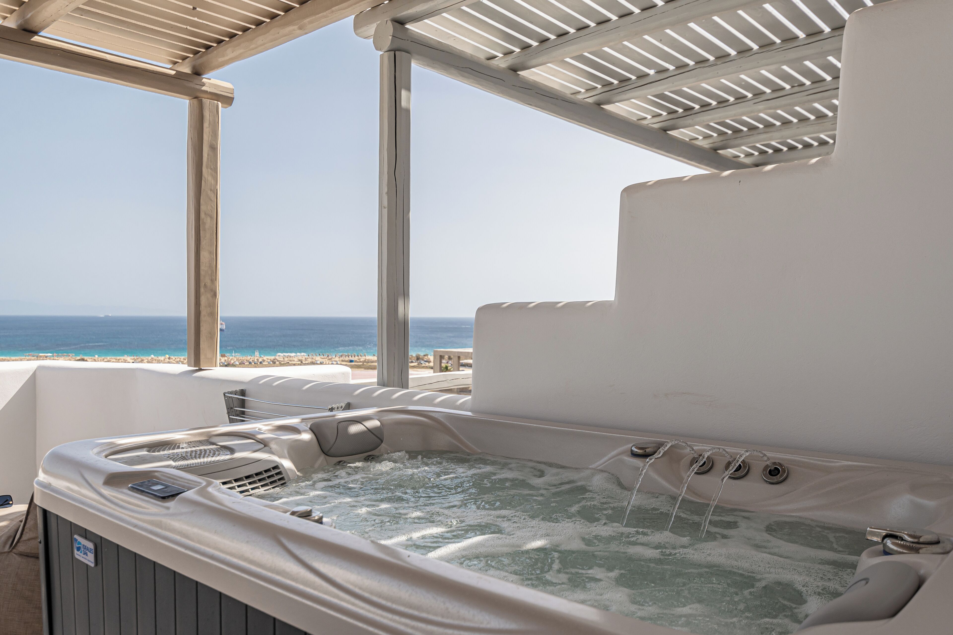 A hot tub with a view of the ocean, under a wooden pergola.