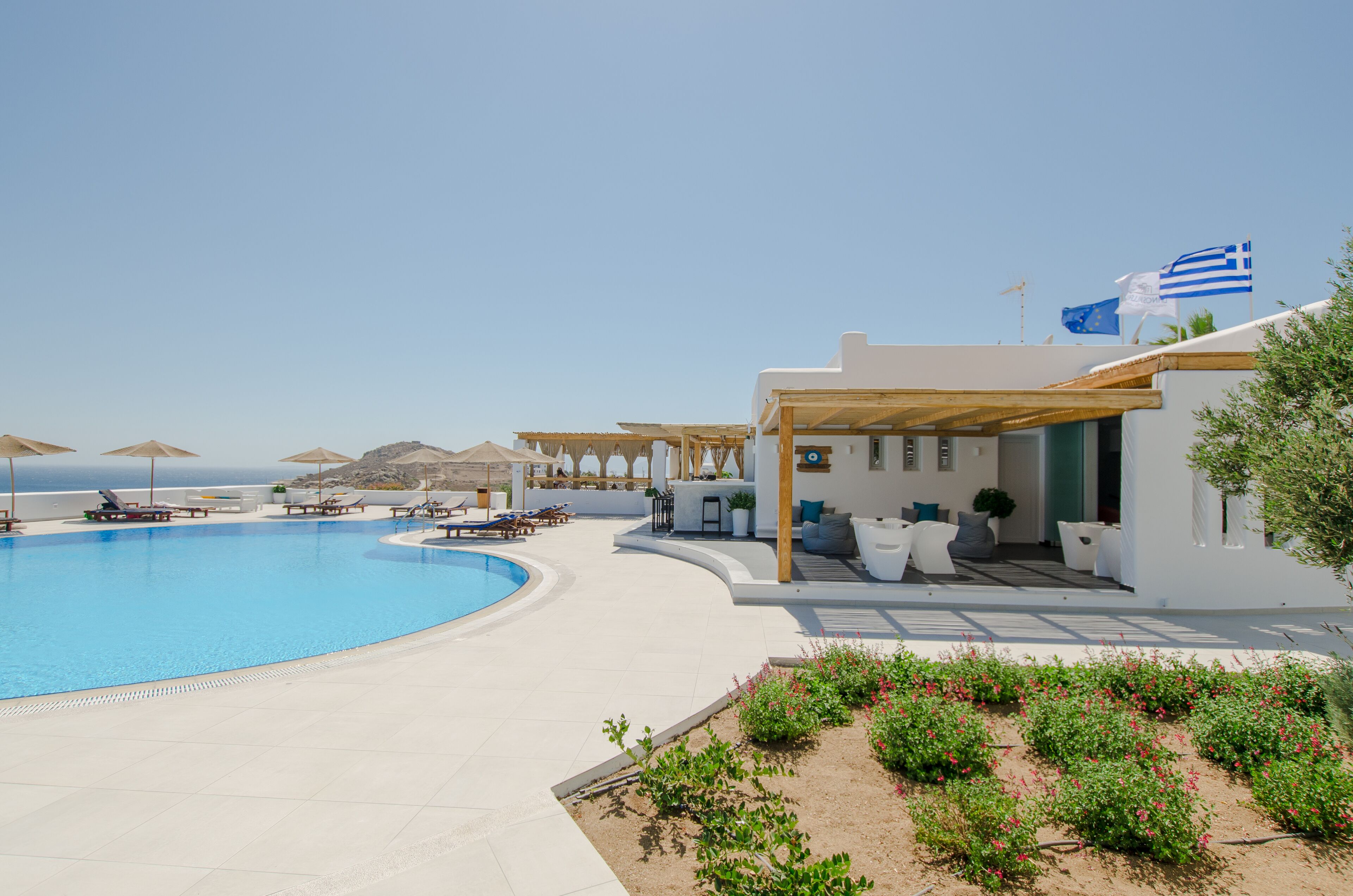 A pool area with lounge chairs and umbrellas, a white building with a flag, and a clear sky.