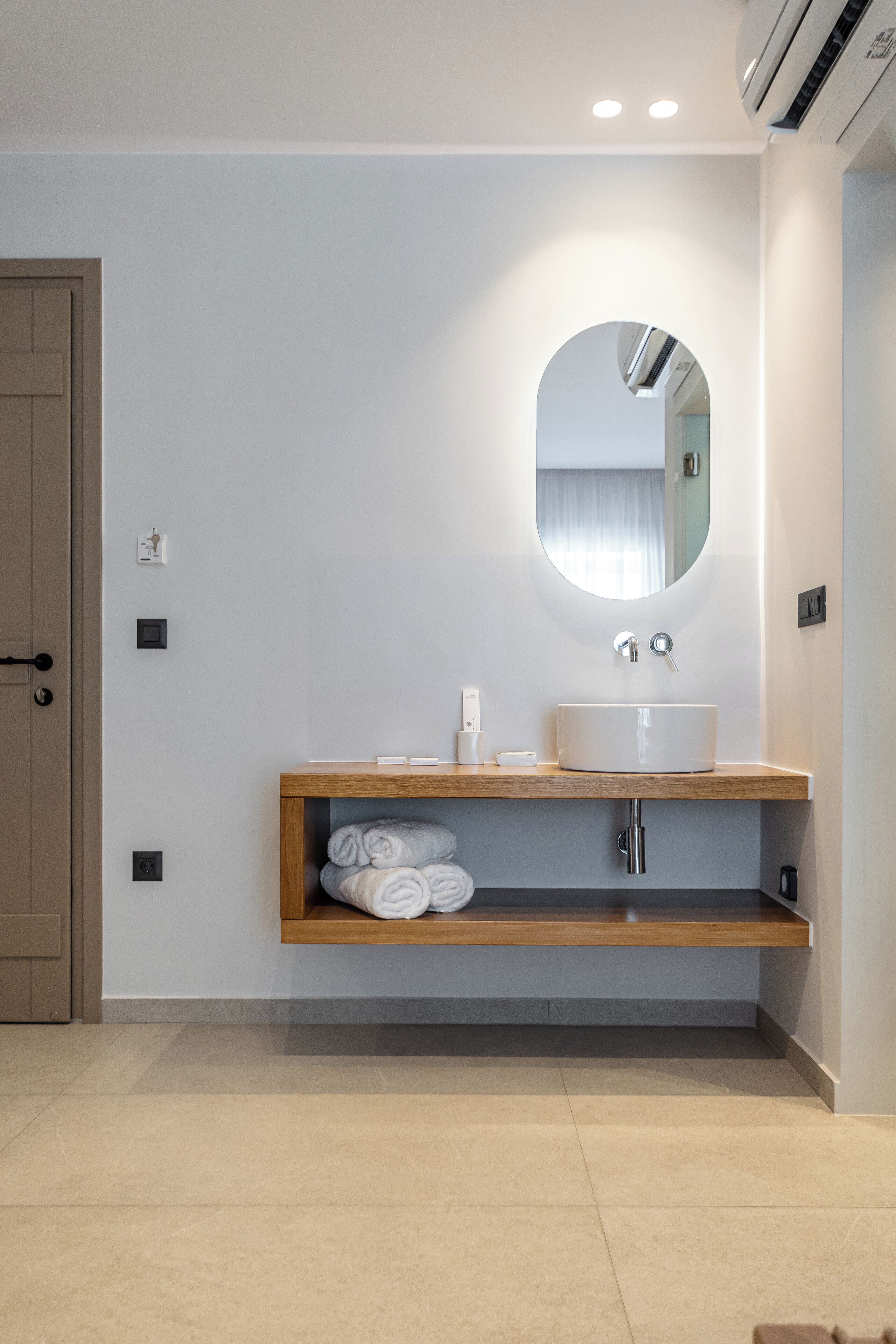 Un baño moderno con un lavamanos blanco, un espejo y un estante de madera con toallas.