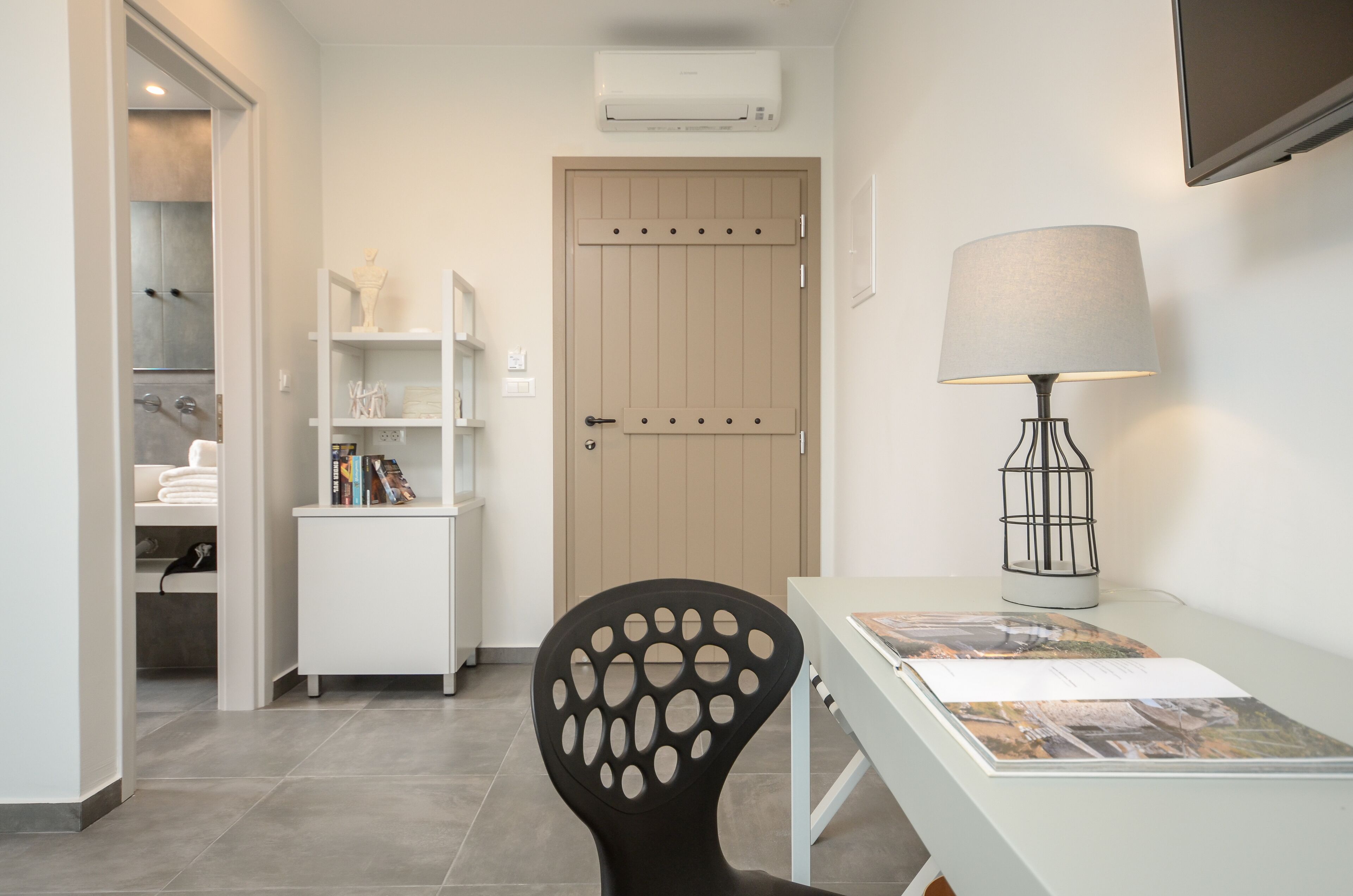 A modern room with a desk, chair, bookshelf, and a door with an air conditioning unit above it.