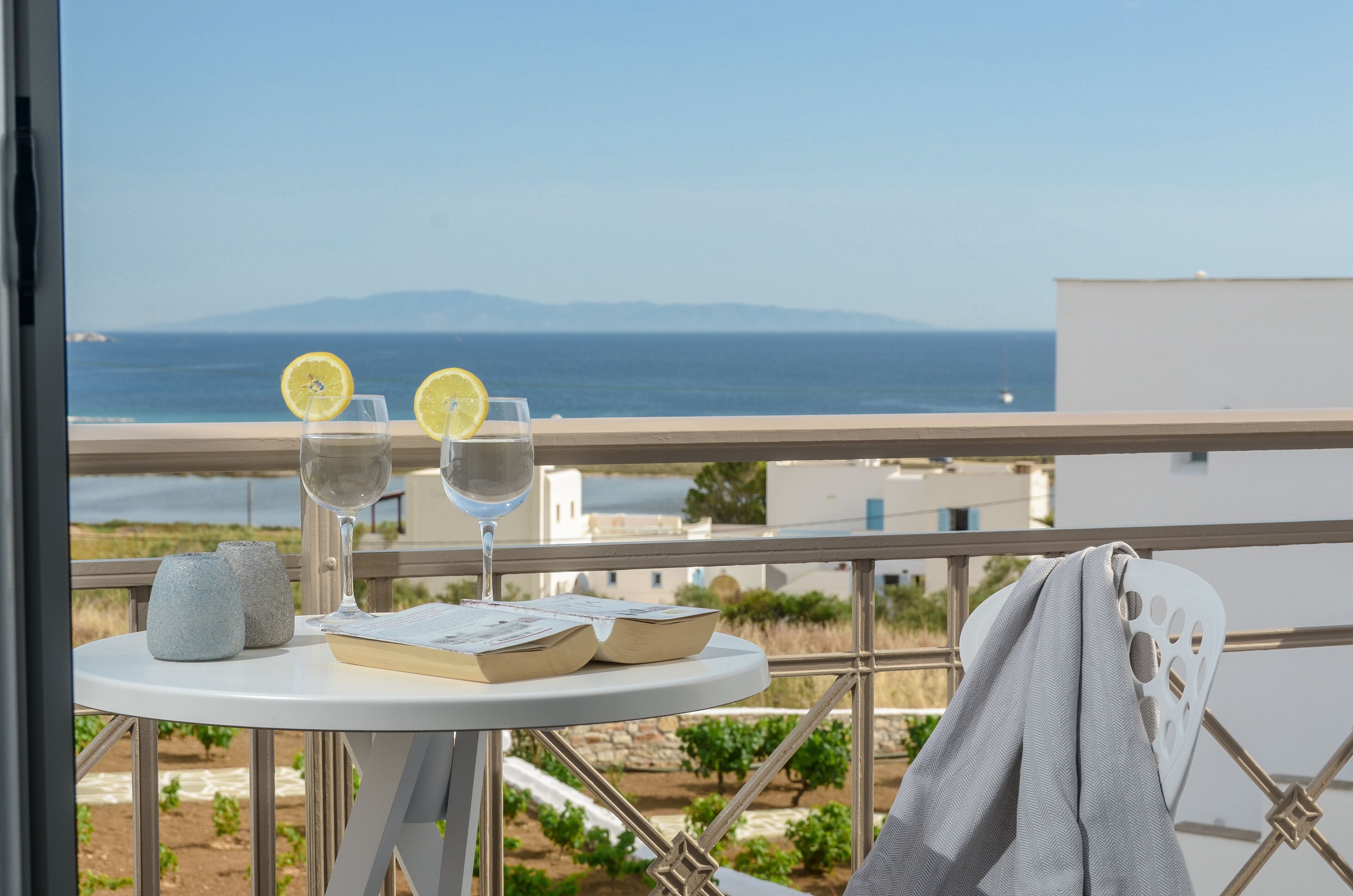 A balcony with a table set for two, featuring two glasses of water with lemon slices, a book, and two small vases.