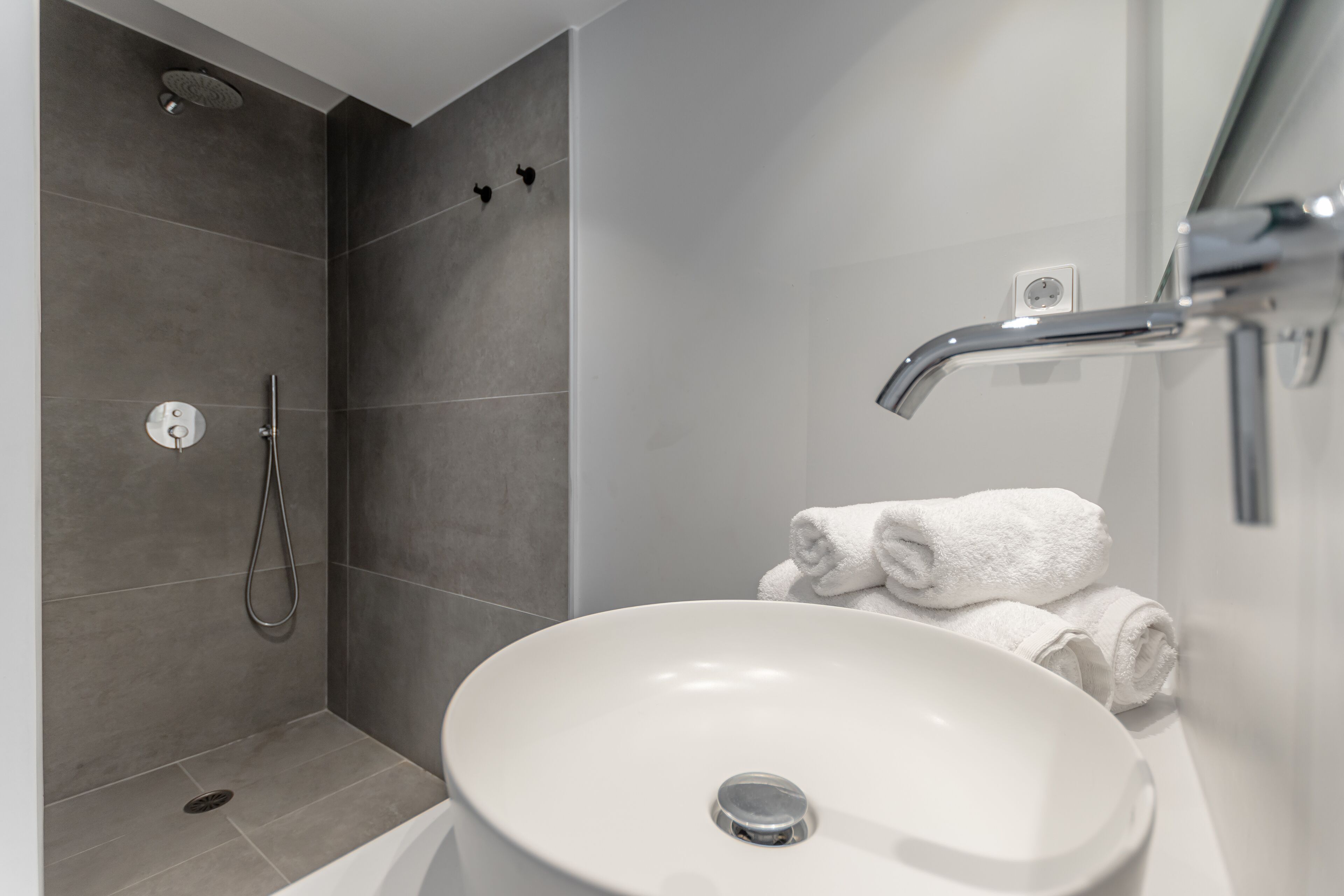 A modern bathroom with a white sink, a shower, and a towel rack.