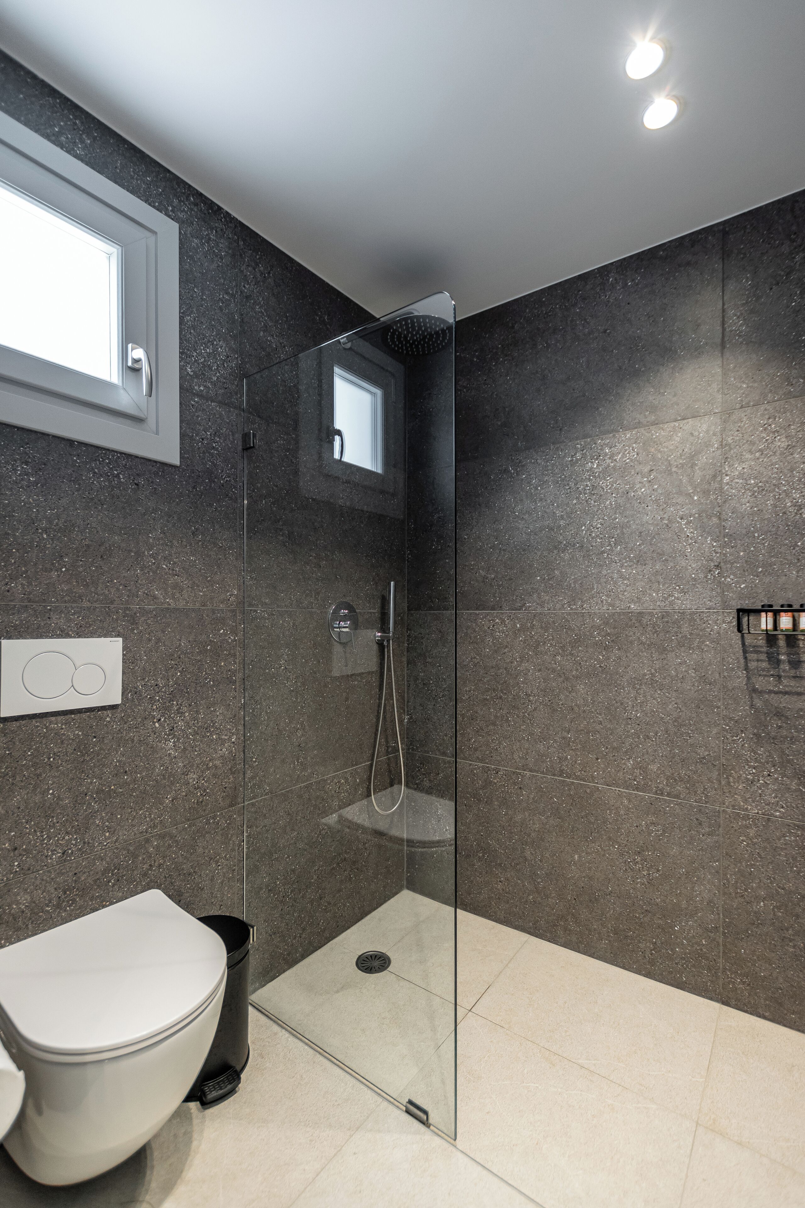 Un baño moderno con ducha envuelta en vidrio, inodoro e iluminación empotrada en la pared.