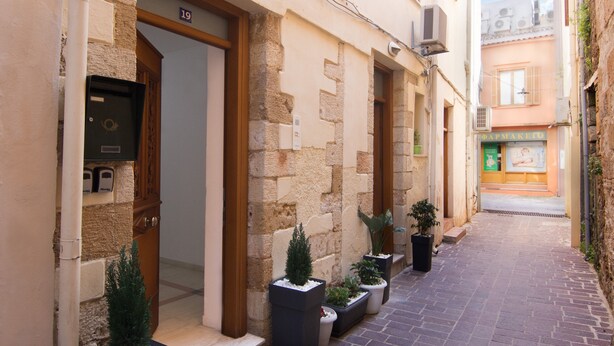 A narrow alley with a building entrance, potted plants, and a visible shop sign. - Daliani Studios Chania (Chania)