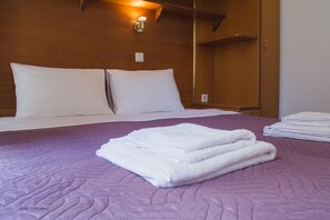 A neatly made bed with white linens and a purple quilted bedspread.