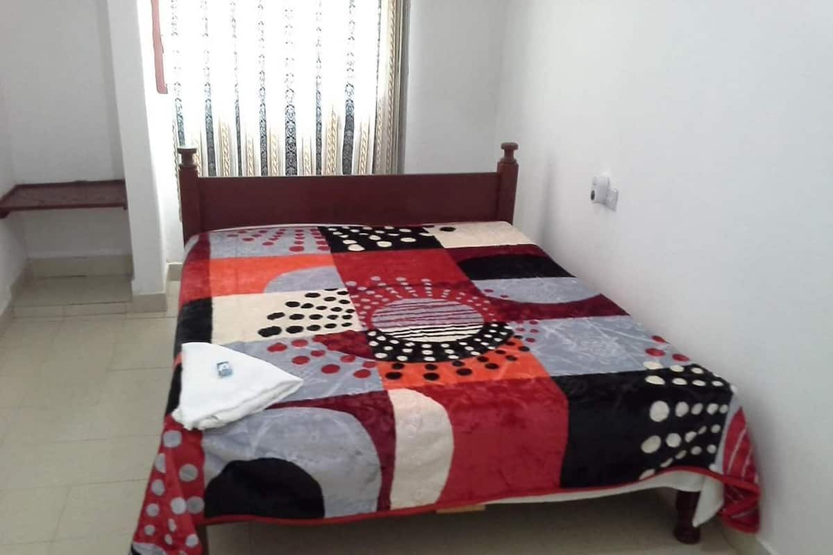 A single bed with a patchwork quilt in a room with white walls and a tiled floor.