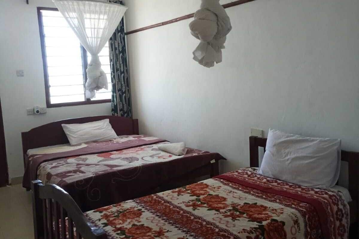 A room with two beds, a ceiling fan, a window with curtains, and a mosquito net.