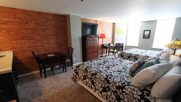 Una habitación con pared de ladrillo, un escritorio, una cómoda, una cama con ropa de cama estampada y una silla.