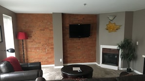 A living room with a brick wall, a flat-screen TV, a fireplace, and leather sofas. - Lodging at the Gaffer Inn (Corning)