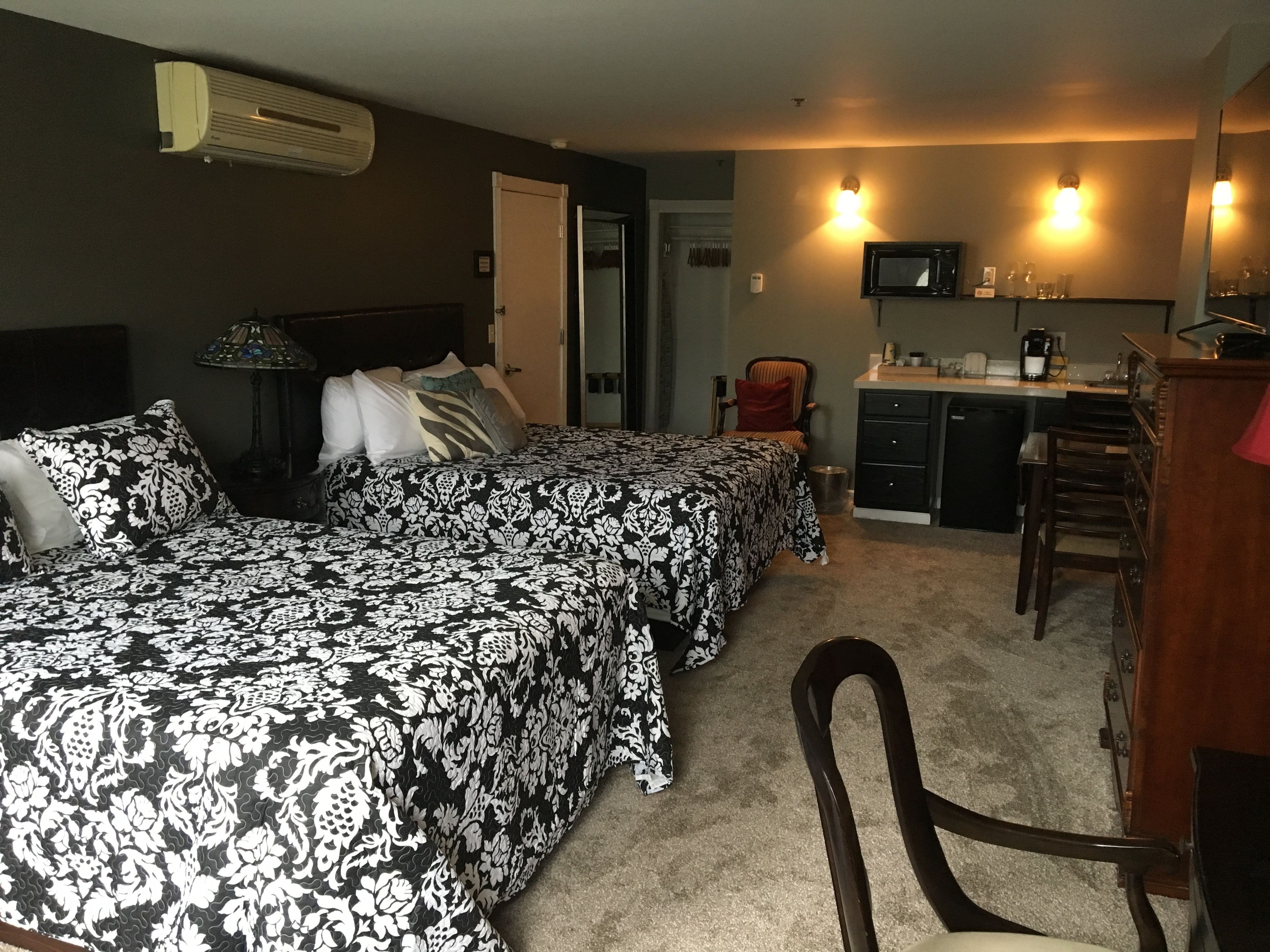 A hotel room with two beds, a desk, a chair, a TV, and a kitchenette.