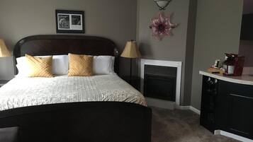 A bedroom with a large bed, a fireplace, a coffee machine, and a framed picture on the wall.