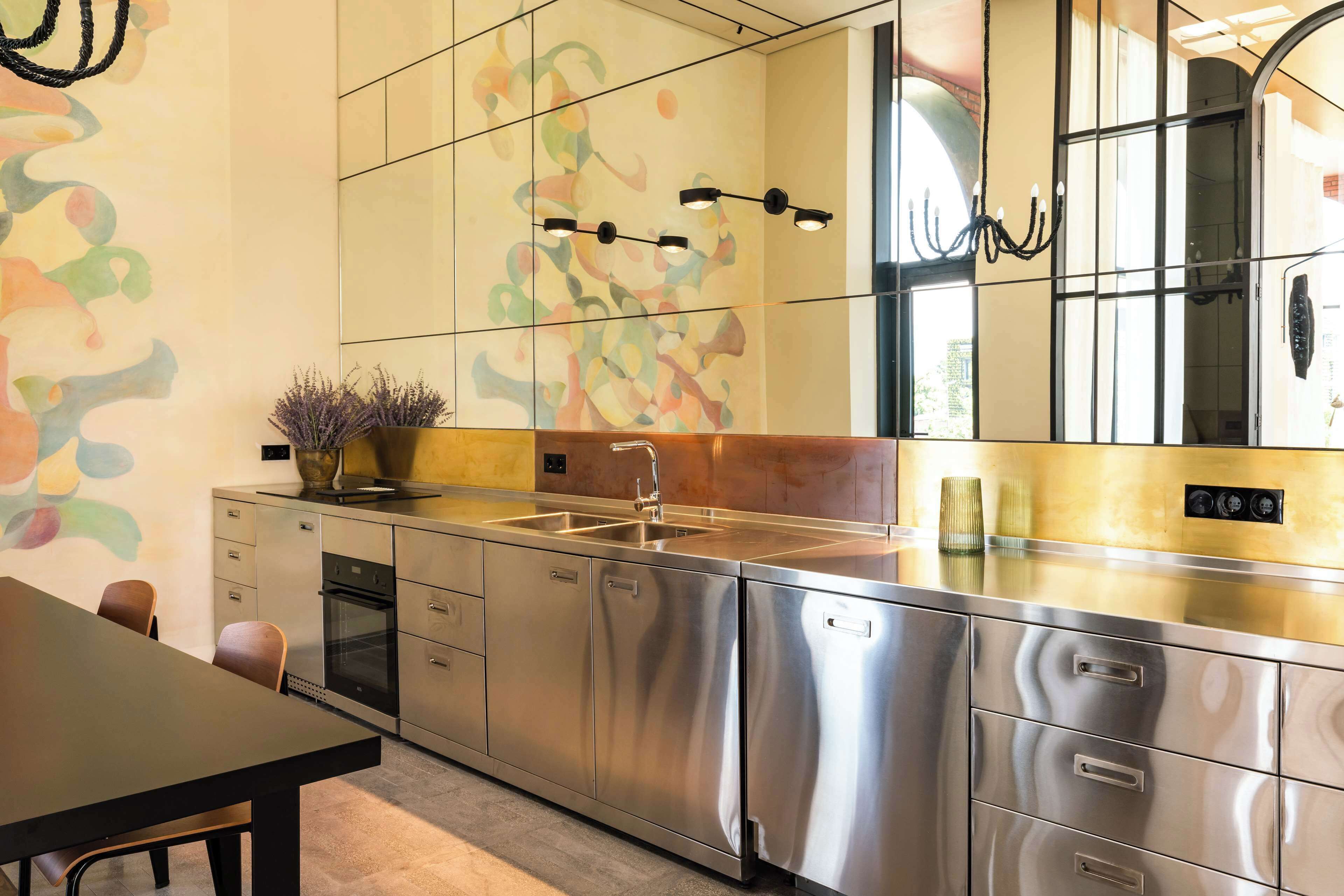 A modern kitchen with stainless steel appliances, a large window, and a colorful abstract wall design.