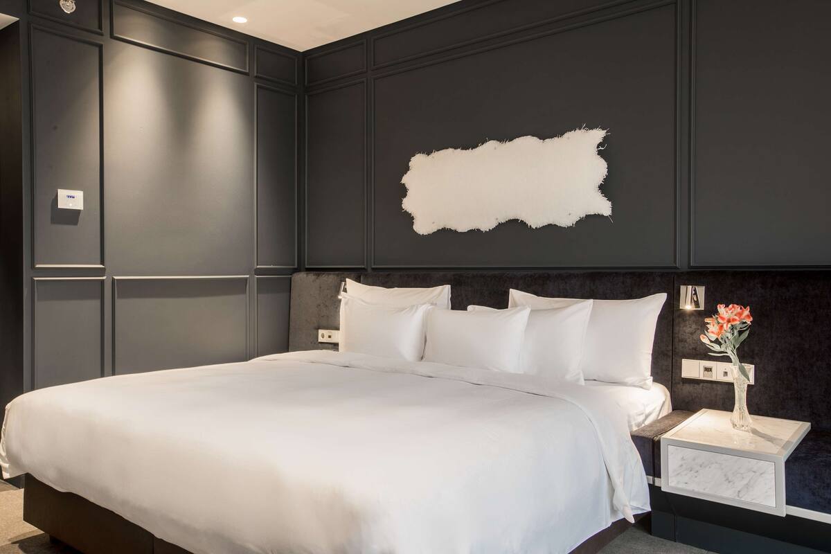A modern bedroom with a large bed, dark wall paneling, and a white accent wall.
