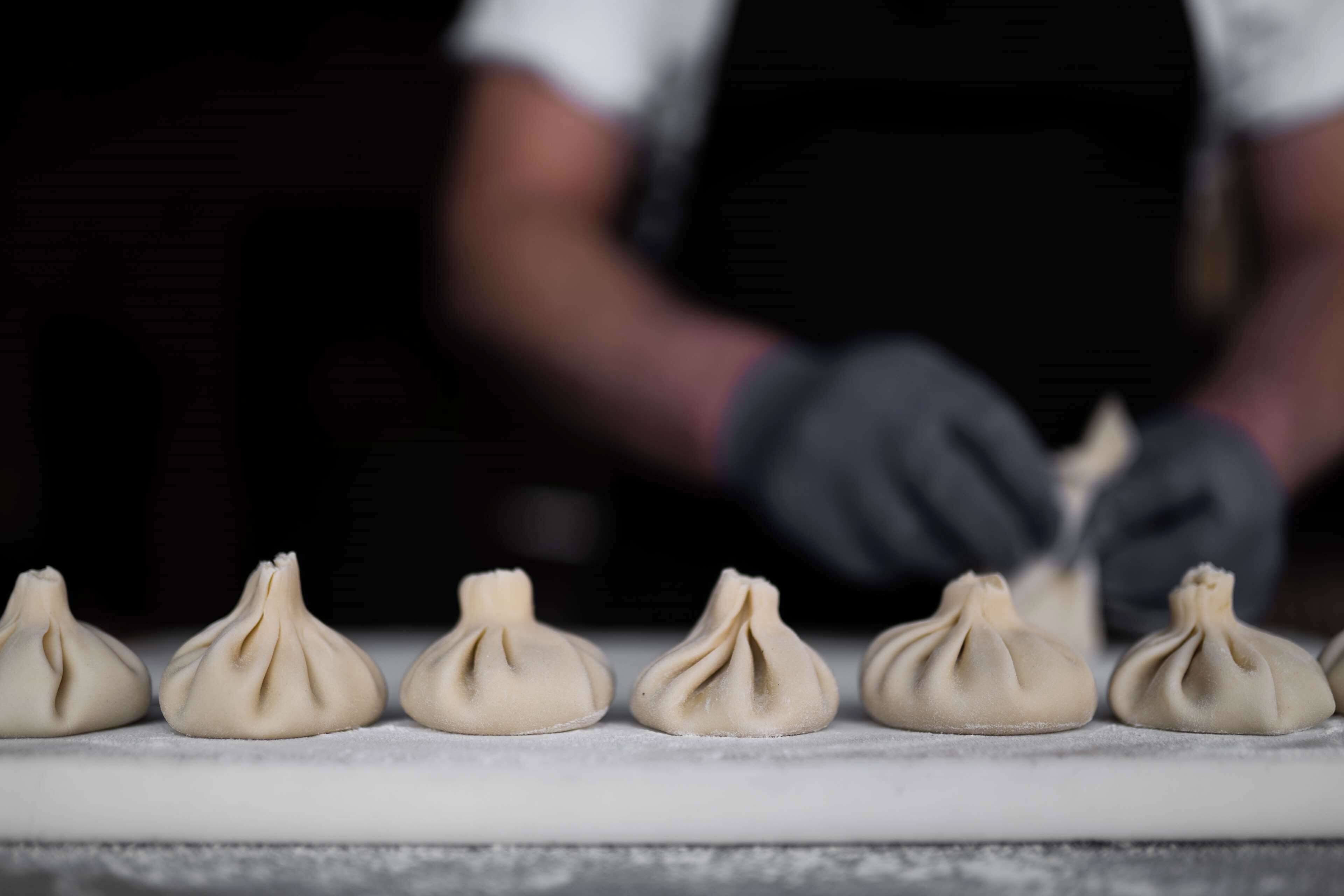 Una persona preparando dumplings sobre una encimera de mármol.