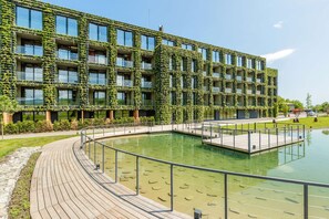 A modern building with a unique facade covered in greenery, a central courtyard with a pool, and a wooden deck surrounding the area.