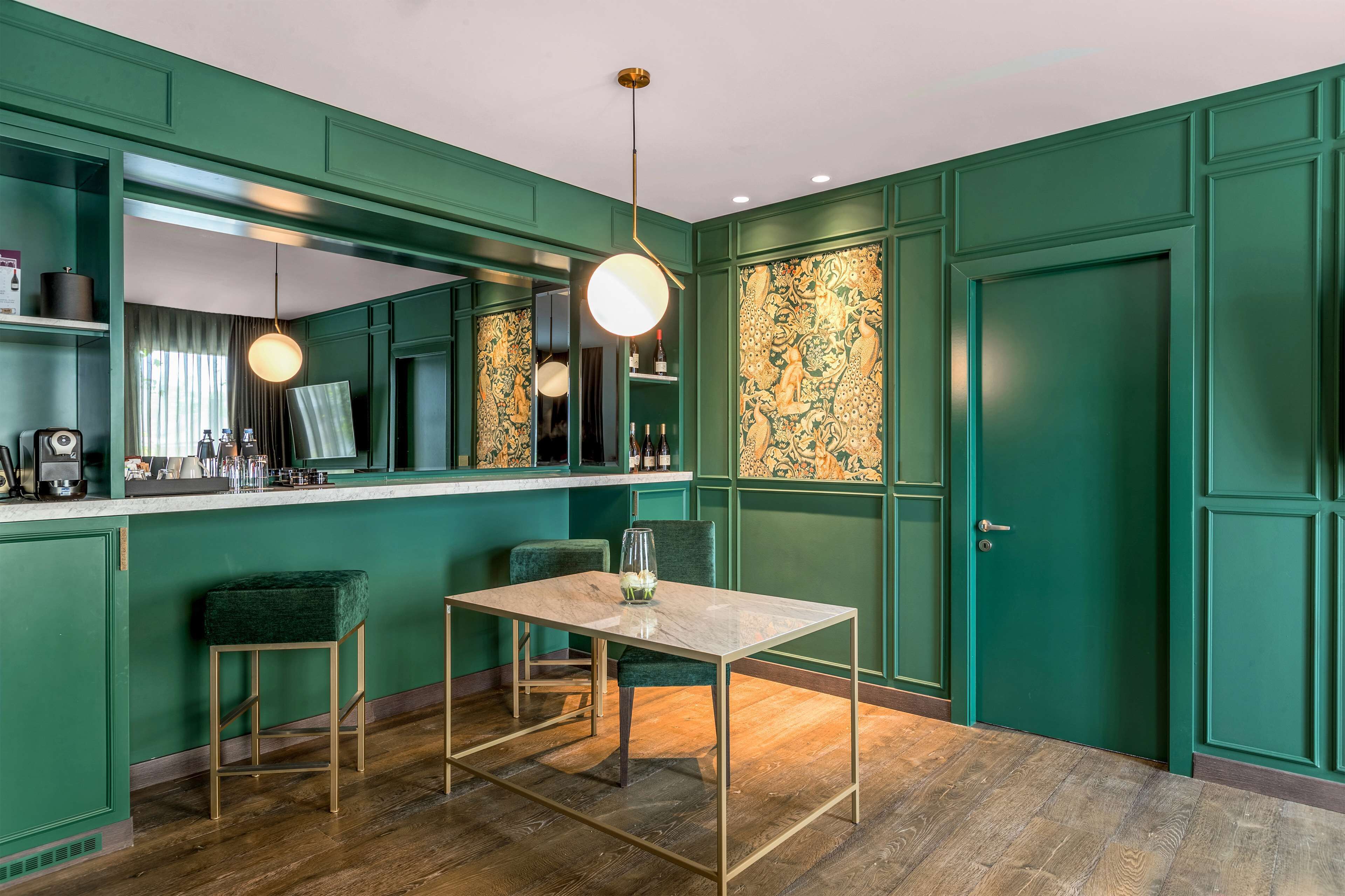 A green-themed room with a marble table, two green chairs, a bar area with a mirror, and a door with intricate artwork.