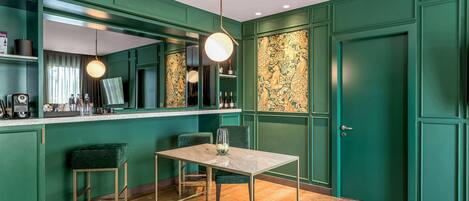 A green-themed room with a marble table, two green chairs, a bar area with a mirror, and a door with intricate artwork.