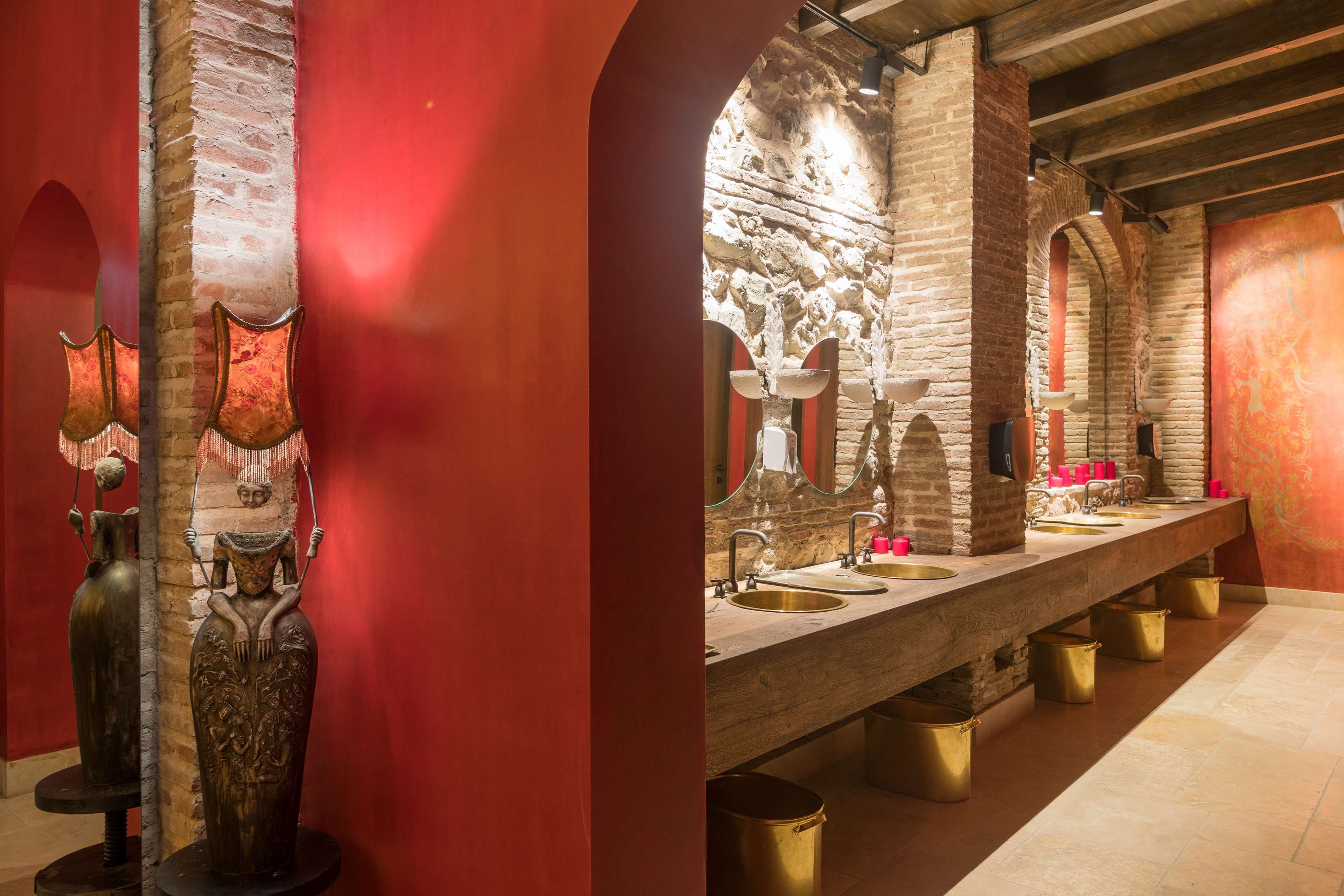 A long, narrow bathroom with multiple sinks and mirrors, stone walls, and decorative vases.