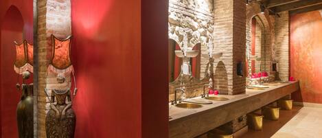 A long, narrow bathroom with multiple sinks and mirrors, stone walls, and decorative vases.