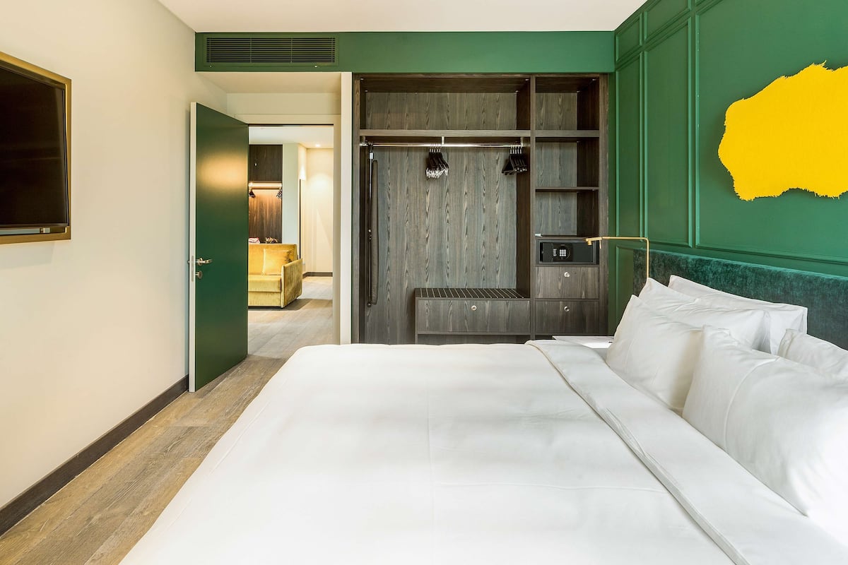 A hotel room with a large bed, a wardrobe with hanging space, and a green accent wall.