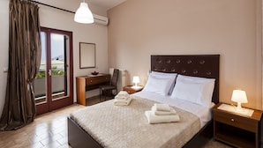 A hotel room with a bed, a desk, a chair, a nightstand, and a window with curtains.
