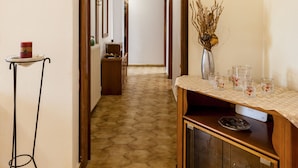 A hallway with a patterned floor, a wooden cabinet with glass doors, and a small table with a vase and glasses.