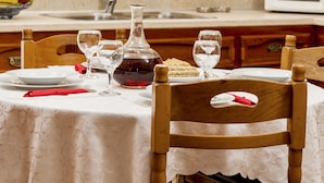A dining table set with plates, glasses, and a bottle, a wooden chair, and a kitchen with a microwave and cabinets.
