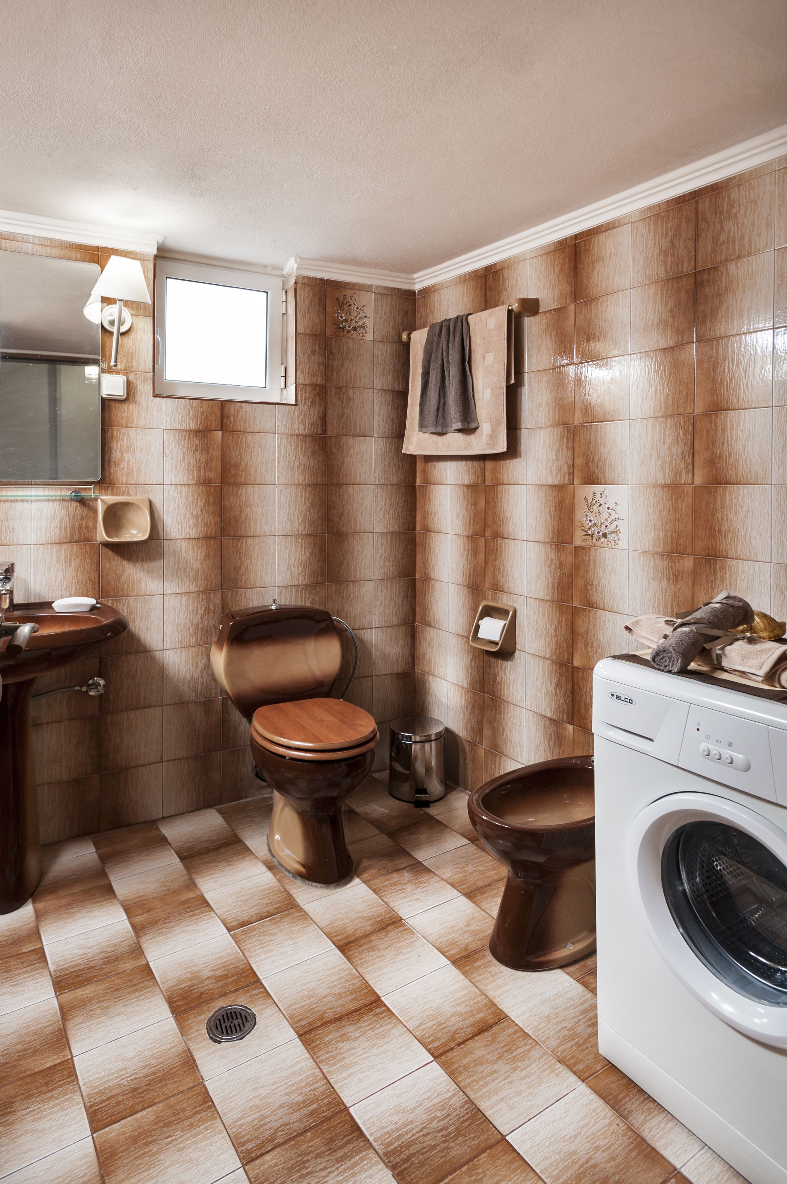 A bathroom with a wooden toilet, a sink, a mirror, a towel rack, and a washing machine.
