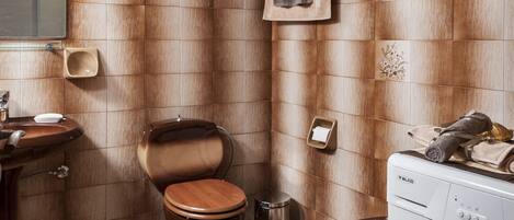 A bathroom with a wooden toilet, a sink, a mirror, a towel rack, and a washing machine.