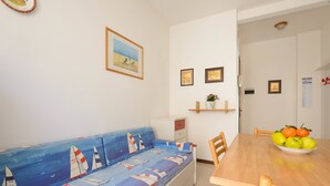 Ein Zimmer mit Schlafsofa, Esstisch mit Stühlen und einer kleinen Ablage mit gerahmten Bildern.