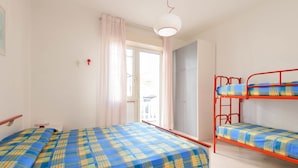Ein Zimmer mit zwei Betten, einem Fenster mit Vorhängen, einem Kleiderschrank und einer Tür, die nach draußen führt.