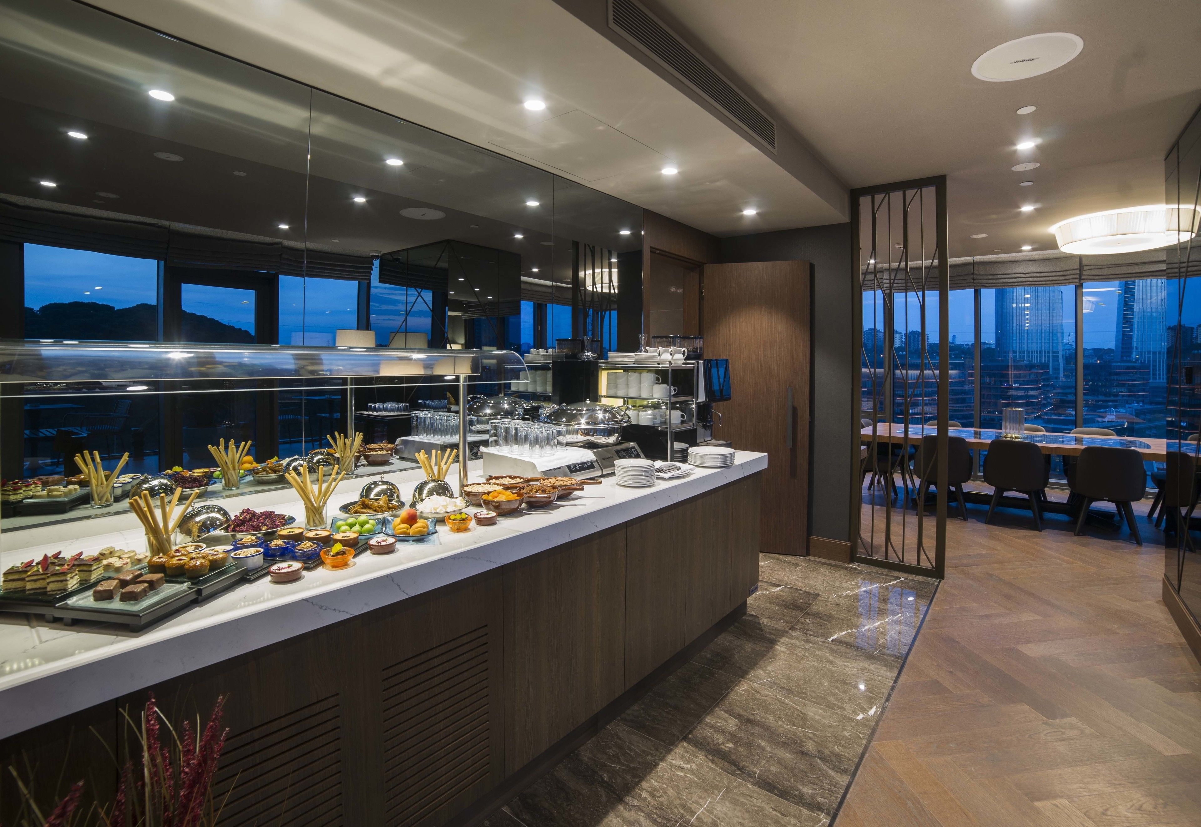 Buffet modern amb una varietat d'aliments i vista a la ciutat a través de grans finestres.