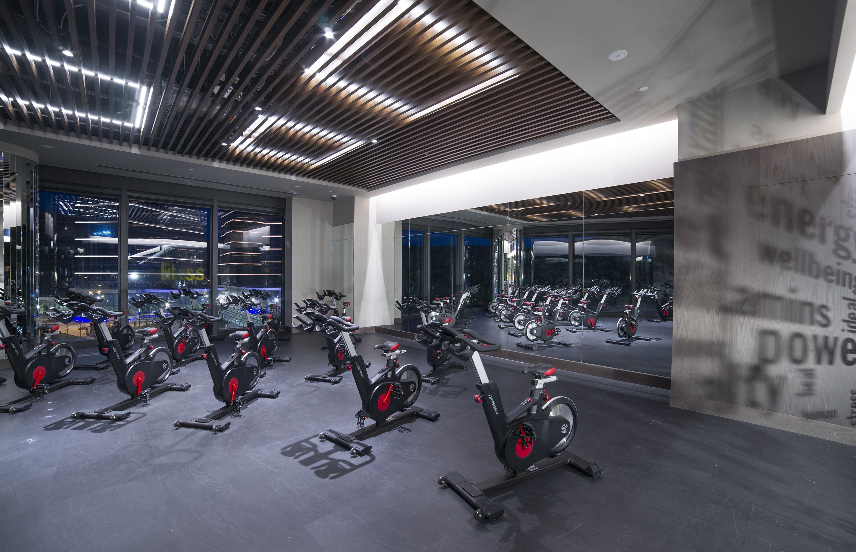 A gym with stationary bikes, large windows, and a modern ceiling design.