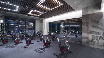 A gym with stationary bikes, large windows, and a modern ceiling design.